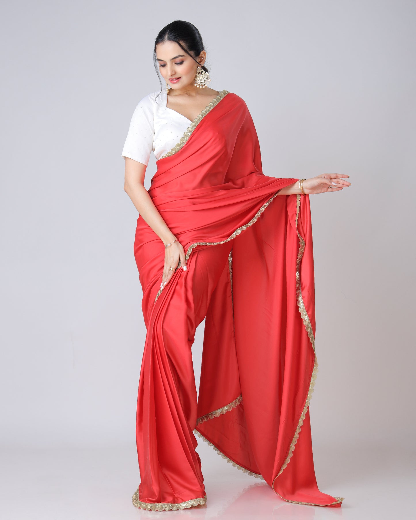 A woman modeling a vermilion red designer saree with romantic lacework and a white blouse. The saree has a solid red appearance with a touch of lace detailing.