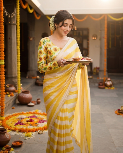 A woman stands in a decorated courtyard holding a tray with food, wearing a yellow and white striped saree with a floral printed blouse. rakshabandhan, festival